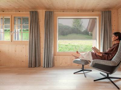A woman is sitting comfortably in an armchair in her wooden house, enjoying the coolness of the room