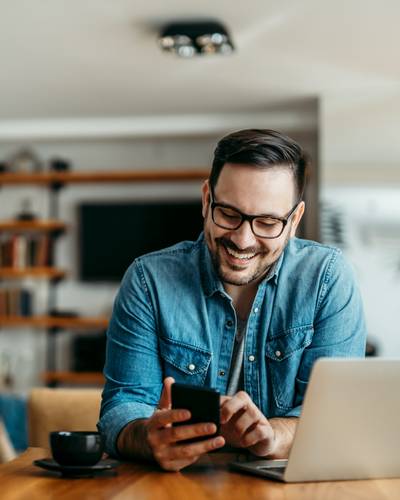 Mann mit Smartphone vor Laptop