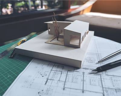 Modelhaus aus Papier auf Plänen liegend zusammen mit Stiften